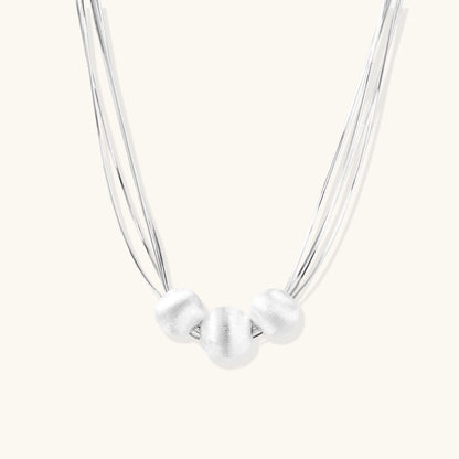 Sterling silver multi-strand necklace with three brushed round beads on cream background