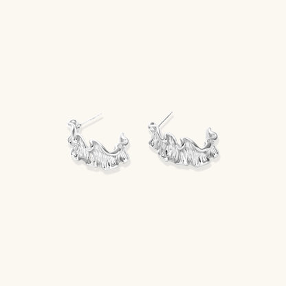 White gold plated sculptural hoop earrings with organic wavy edges and reflective metallic finish on cream background